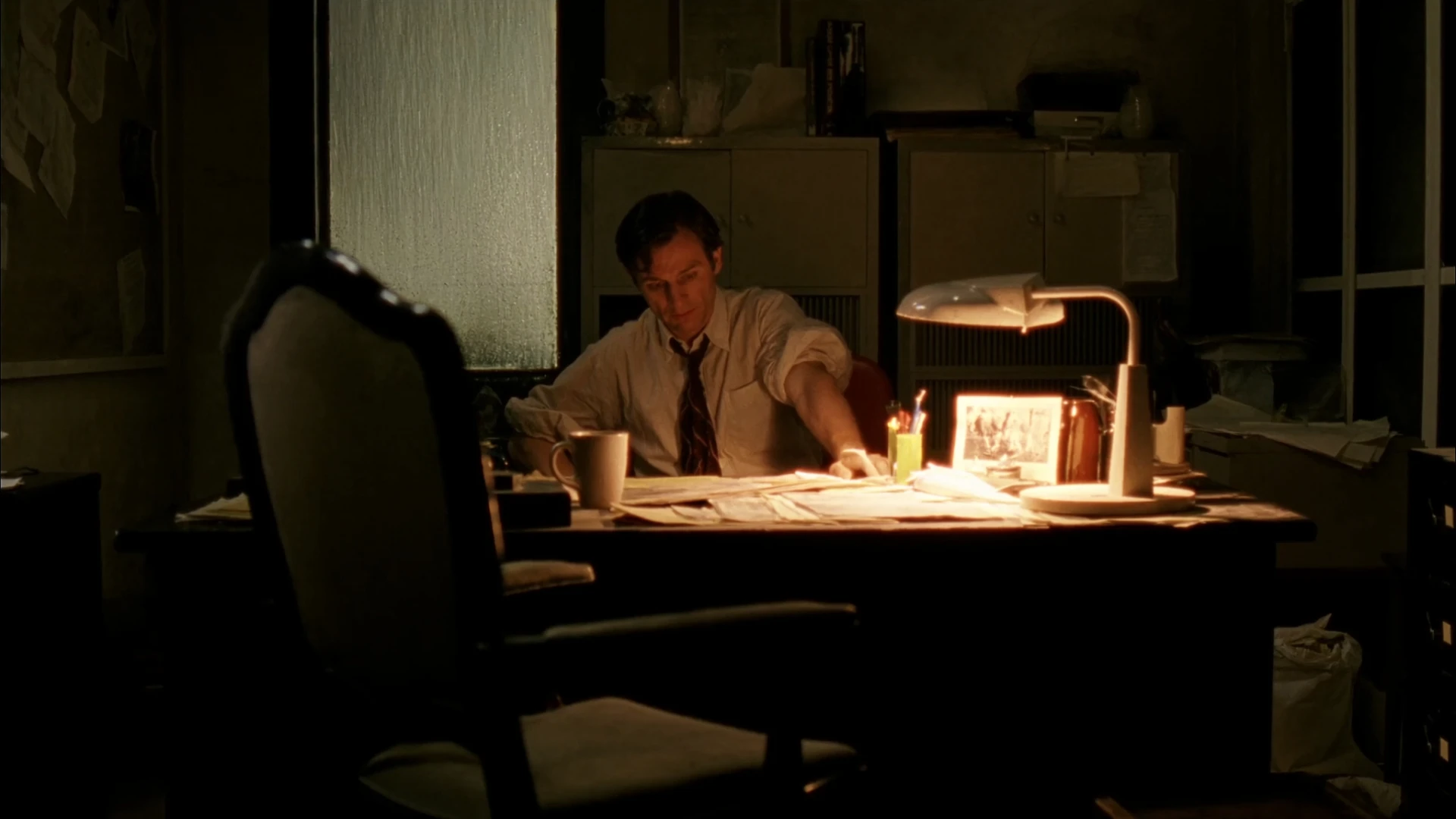 CASE85 investigator working late at a desk beside an empty chair during the Kentucky real estate broker search.